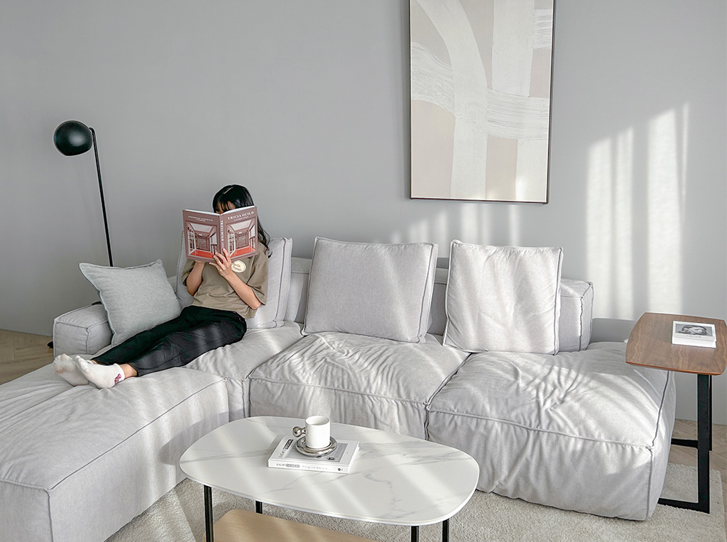 超高包覆、寬廣坐深,釋放全身疲勞 一人坐在格雷沙發看著書,雙腿放在沙發腳椅上