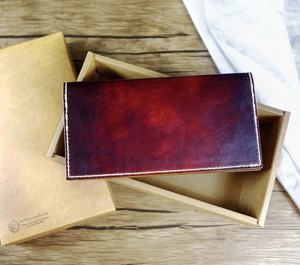 簡約長夾課程完成作品外觀,紅棕色植鞣革長夾關閉狀態,平放於牛皮紙盒上展示皮革染色質感
