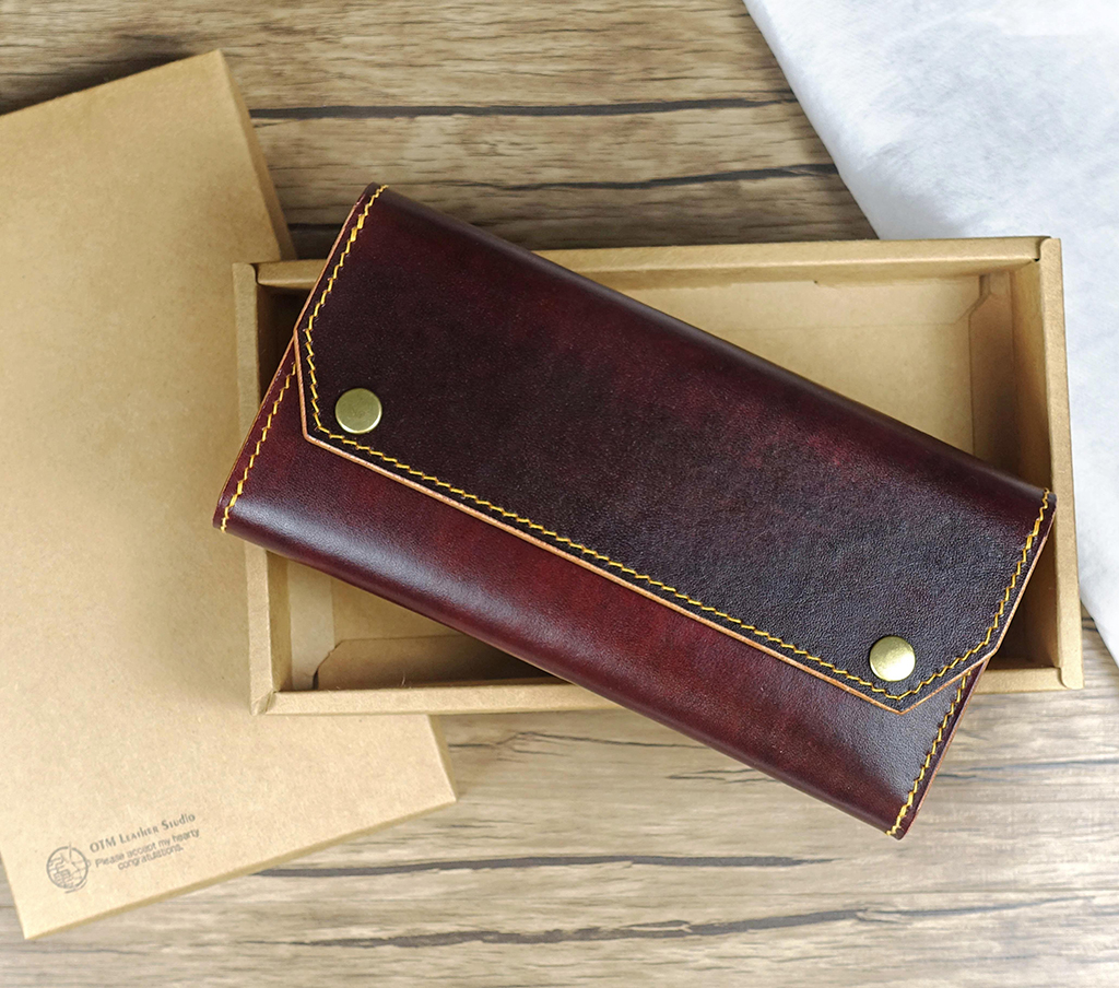 風琴長夾翻蓋外觀實拍,深酒紅色植鞣革長夾置於紙盒中,翻蓋設計搭配金色釦件與手縫線細節,呈現完整正面比例