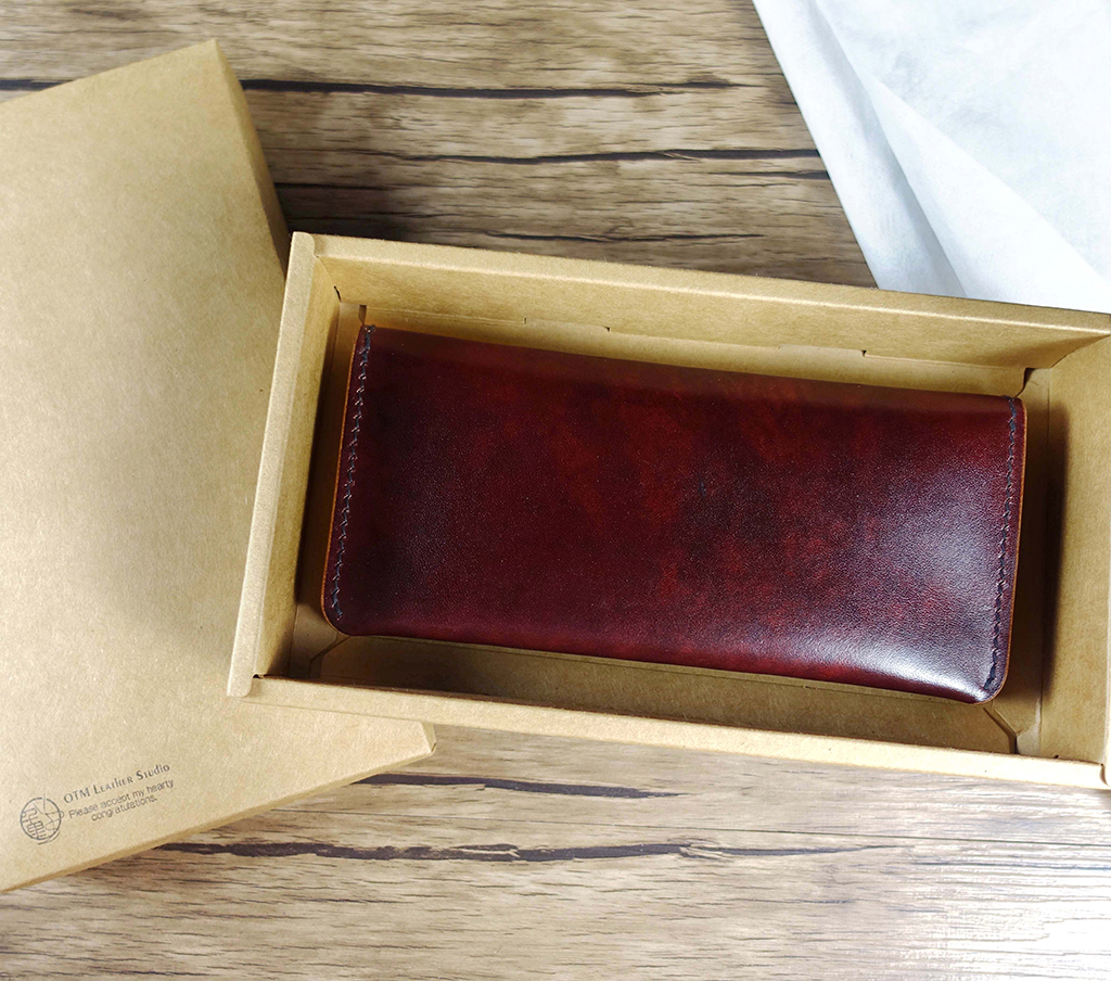 折疊外皮設計的風格長夾,合起後呈現自然曲線外型,放置於牛皮紙包裝盒中,展現俐落且偏男性風格的長夾設計。