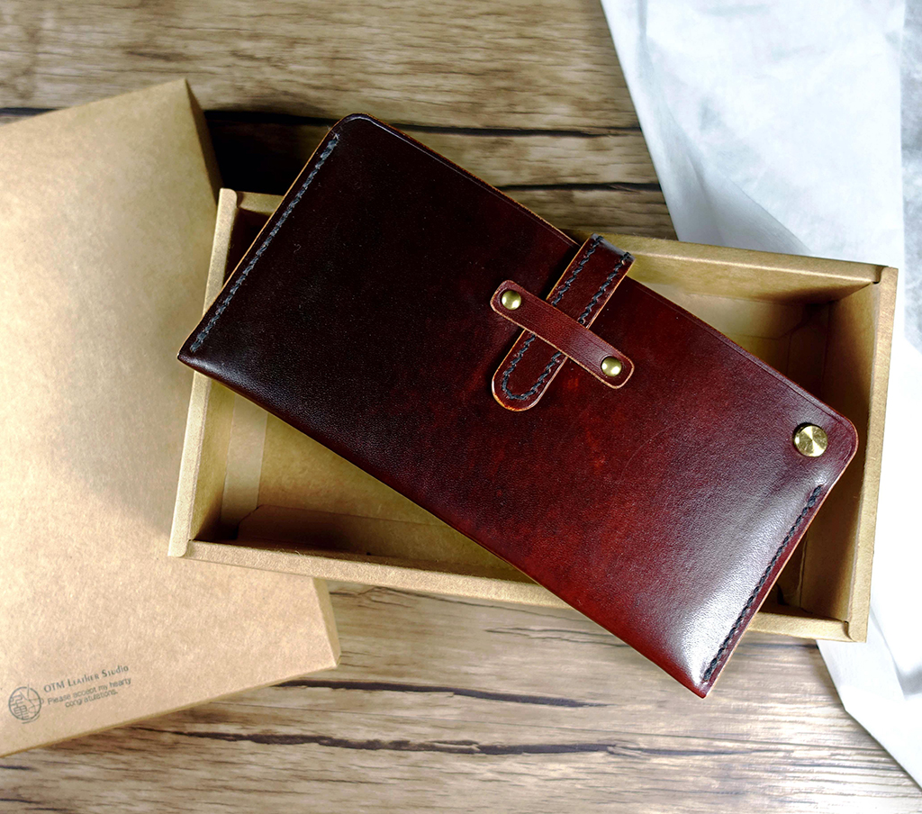 翻轉長夾外觀展示,紅棕色植鞣革長夾搭配金屬螺絲扣與固定皮帶設計,收納後比例俐落穩重。