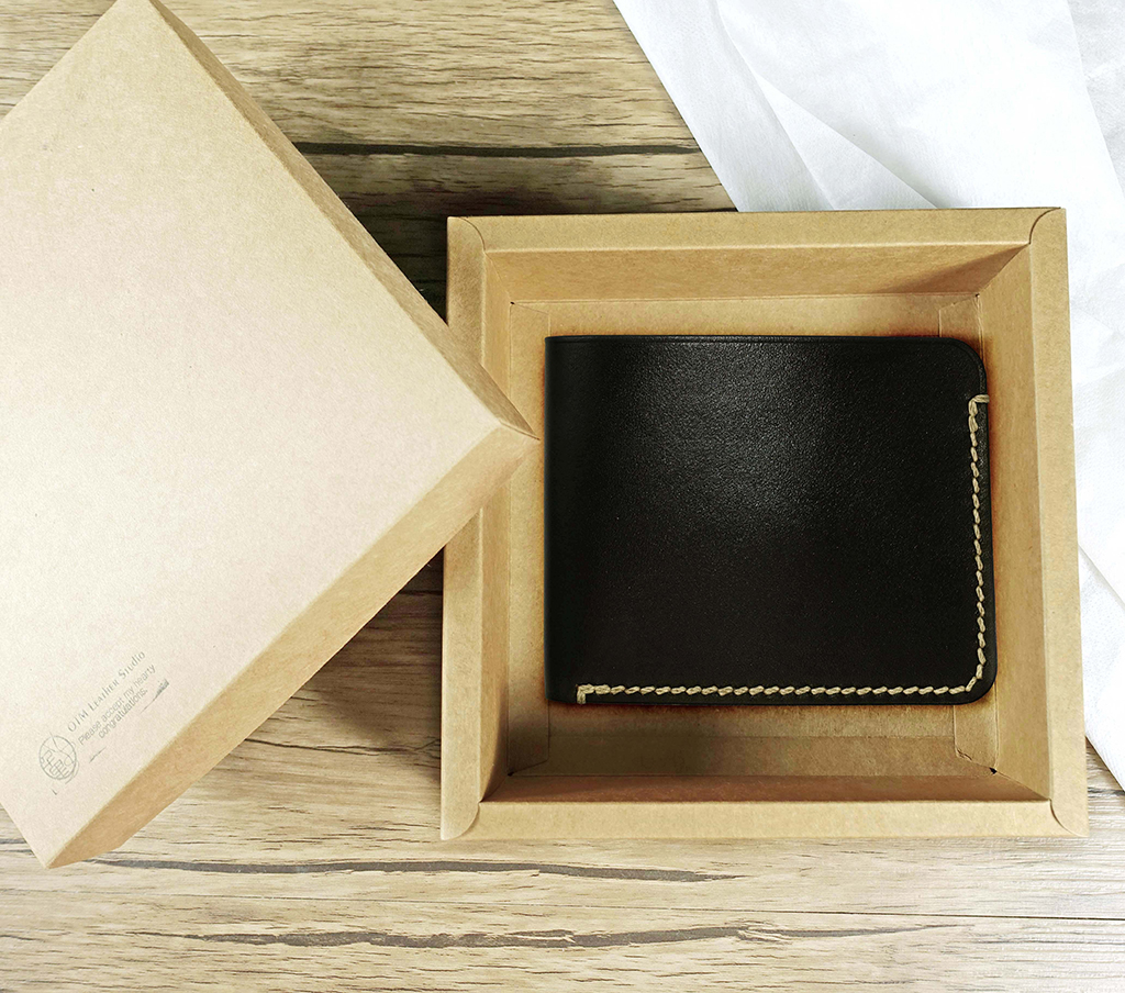 兩片簡約短夾黑色款放置於牛皮紙禮盒內,外層為純黑植鞣革,外圈手縫收邊明顯,呈現極簡薄型口袋比例設計與送禮包裝情境。