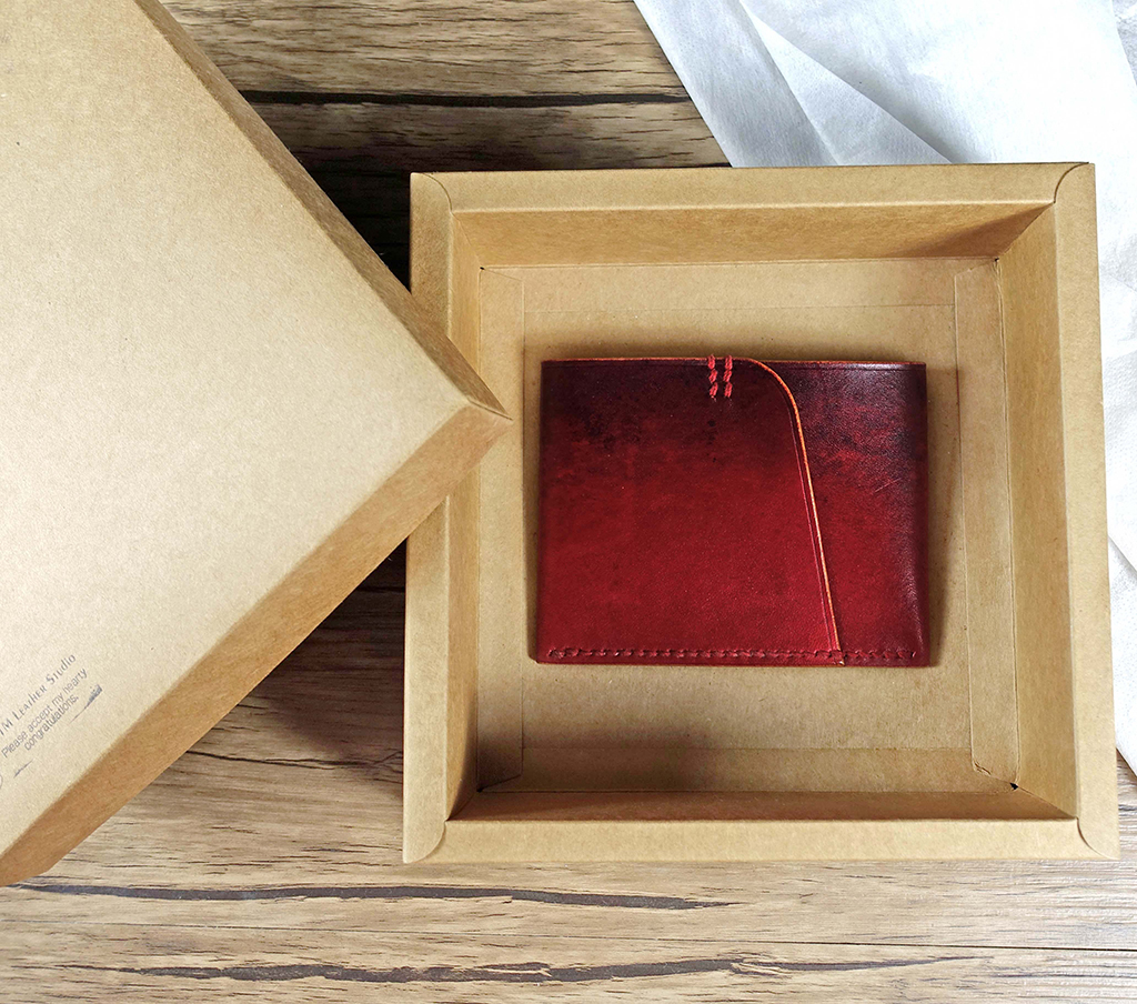 單片短夾紅色款置於牛皮紙禮盒內,單片皮革折疊成形,外圈手縫收邊細節清楚,呈現極簡輕薄口袋比例與送禮情境。