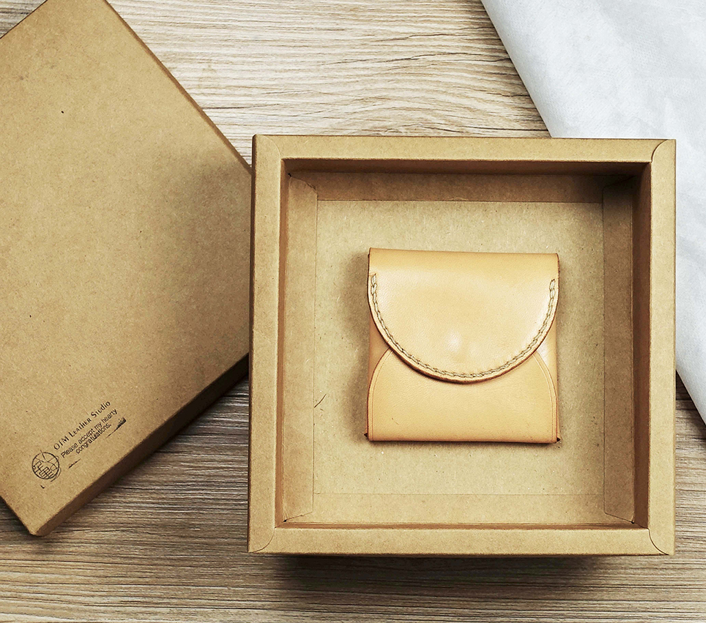 外方內圓零錢包課程完成作品,植鞣革零錢包放置於牛皮紙禮盒中,方形外觀搭配圓弧翻蓋設計。