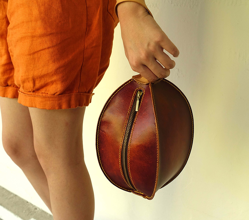 球型手拿包課程成品示範,義大利植鞣革立體球型包款,弧形拉鍊設計,手持提把外出使用情境照。