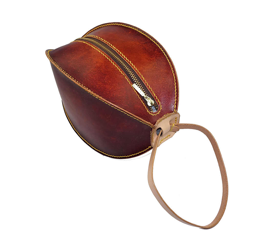 立體球型手拿包俯視角度展示,弧形金屬拉鍊與曲面拼接結構細節,植鞣革漸層色澤呈現。