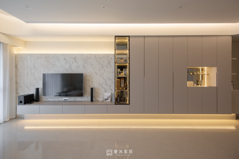 客廳展示櫃搭配間接照明，結合大理石紋電視牆與整面系統櫃，呈現溫暖細膩的夜間氛圍