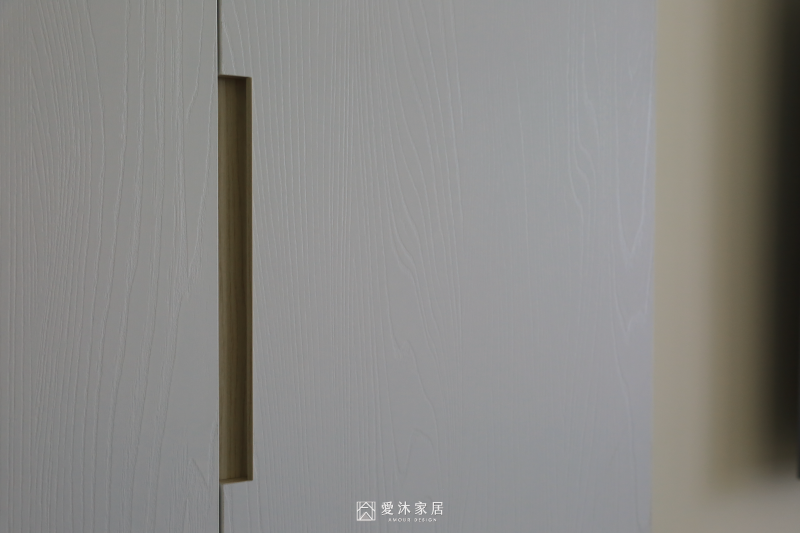 客廳白色木紋系統櫃門片與內嵌式把手細節，呈現簡潔俐落的櫃體設計