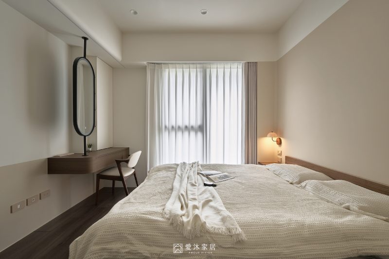 主臥以暖白與胡桃木色調營造簡約溫潤氛圍，窗邊規劃懸浮化妝桌與橢圓鏡，搭配自然採光打造舒適休憩空間