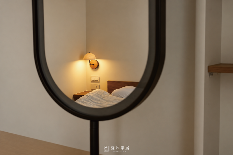 從橢圓化妝鏡反射主臥床頭洞石壁燈與木質床頭設計，以鏡面視角呈現臥室柔和溫潤的休憩氛圍