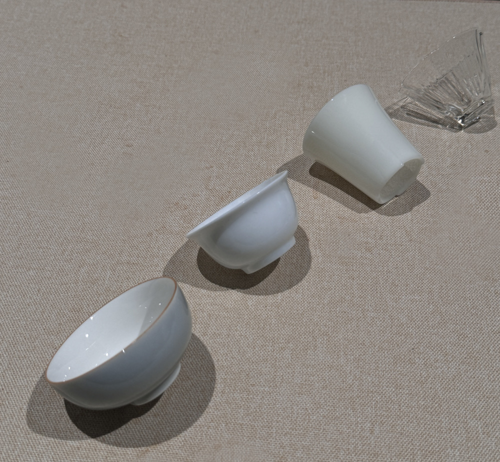 四款茶杯，分別是寬口青灰色，撇口白瓷、羊脂玉瓷高杯、透明玻璃蓮花杯