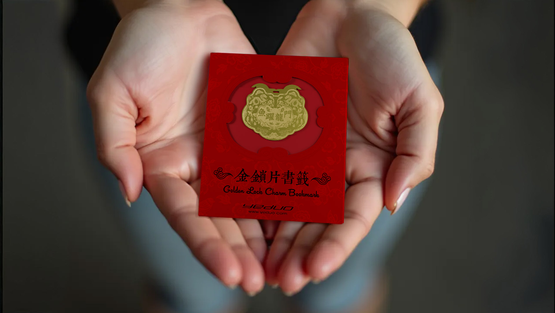 葉朵 YEDUO 金鎖片系列書籤：魚躍龍門單入組。精緻的金色鏤空金屬書籤，刻有「魚躍龍門」吉祥字樣與雙龍抱魚圖案，放置於正紅色喜慶包裝袋中，由雙手平托展示，寓意學業進步、事業高升。